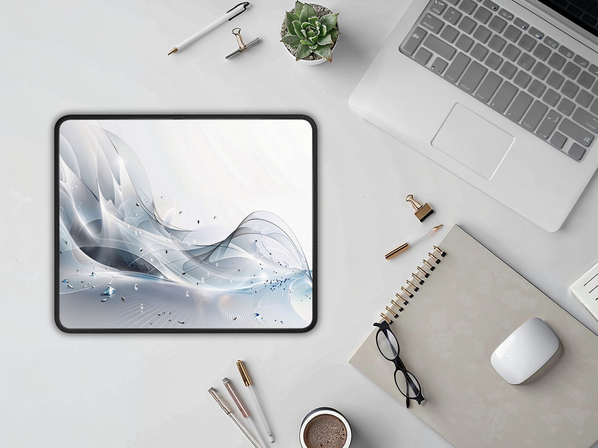 Overhead view of the mouse pad by a laptop and stationery on a clean, white surface.