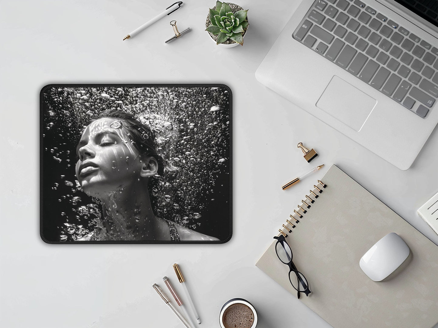 Mouse pad on a white desk with a laptop, notebook, glasses, and a white mouse, highlighting a detailed water droplet design.