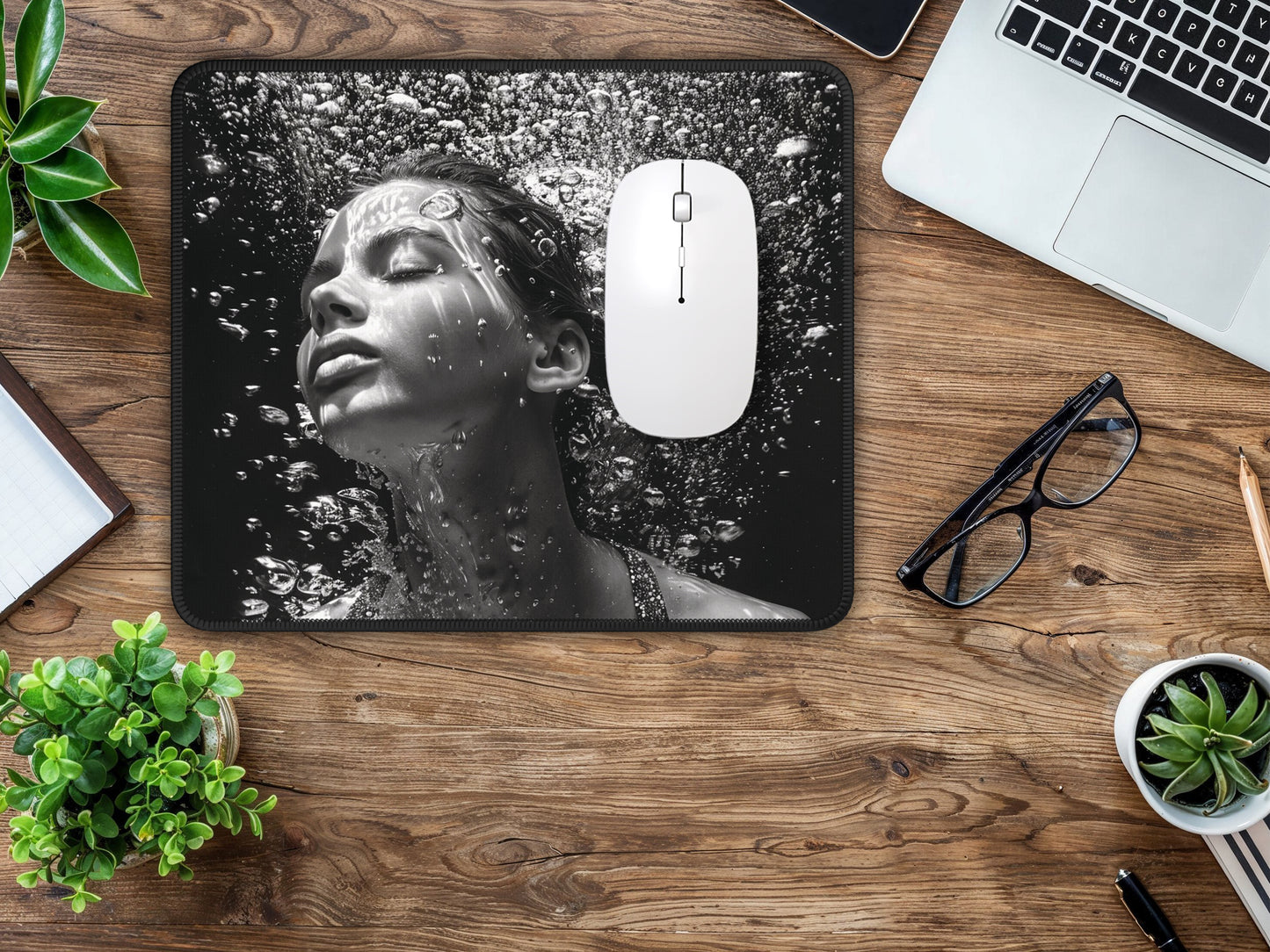 Mouse pad on a wood-textured desk with a laptop and glasses, featuring a striking image of a woman in water, in shades of grey.